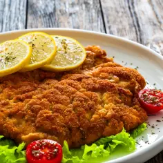 Złocisty kotlet schabowy Magdy Gessler, podany z cytryną i pomidorkami, na liściach sałaty.
