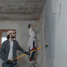 Para malują ściany, tworząc subtelne paski. On z wałkiem w ręku, ona na drabinie.