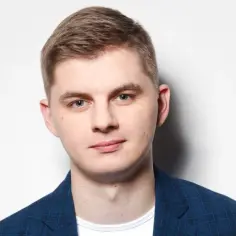 Młody mężczyzna w niebieskiej marynarce w kratę, pewny siebie, jakby miał zaraz wygłosić przemówienie.