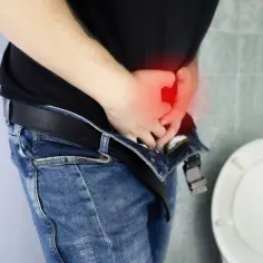 Mężczyzna z bólem w podbrzuszu, szuka najskuteczniejszego antybiotyku na zapalenie prostaty. Obok widoczna muszla klozetowa.