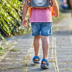 Dziecko w plecaku idzie chodnikiem, rozpoczynając swój szkolny obowiązek.