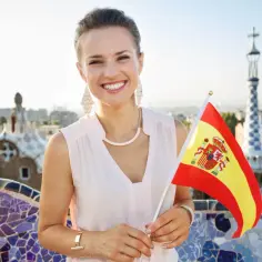 Uśmiechnięta kobieta z flagą Hiszpanii w Parku Güell w Barcelonie. Zastanawia się, ile trwa lot do Barcelony z Krakowa.