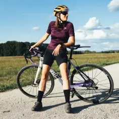 Kobieta w kasku i stroju kolarskim opiera się o rower crossowy, gotowa do jazdy. Idealny sprzęt do testowania w rankingu rowerów crossowych.