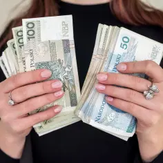 Dłonie trzymające pliki polskich banknotów 100 i 50 zł. To może być nagroda jubileuszowa za lata pracy.