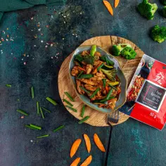 Pyszny kurczak po kantońsku z warzywami, obok paczka pasty do stir-fry.