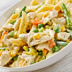 Penne z kurczakiem i warzywami w kremowym sosie. Danie zawiera zieloną fasolkę, groszek, kukurydzę i marchewkę.