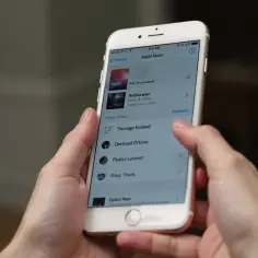 Ręce trzymające iPhone'a z otwartą aplikacją Apple Music, pokazującą listę utworów. Dowiedz się, jak pobrać muzykę na telefon.