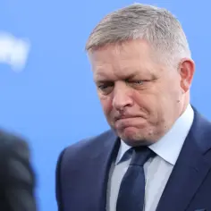 Premier Słowacji w garniturze, z zamyśloną miną, na tle niebieskiego tła.
