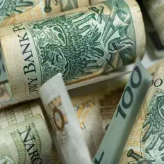 Zwijane banknoty 100 zł, symbolizujące wsparcie finansowe, jak zasiłek rodzicielski, tworzą stos pieniędzy.