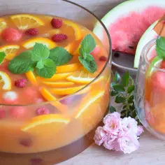 Szybki poncz alkoholowy z pomarańczą, malinami i arbuzem, ozdobiony miętą. Idealny na letnie przyjęcie.