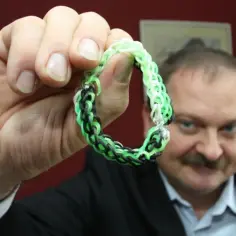 Mężczyzna trzyma bransoletkę z gumek w kolorach zielonym, czarnym i białym. Czy bransoletki z gumek są szkodliwe?