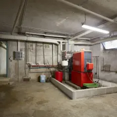 Czerwony piec na ekogroszek w kotłowni z rurami i oświetleniem.