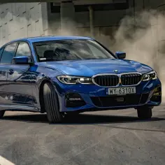 Niebieskie BMW 330i xDrive w zakręcie, unosząc tumany kurzu.
