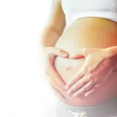 Dłonie tworzą serce na brzuchu kobiety w ciąży. To piękny symbol miłości i oczekiwania na nowego członka rodziny.