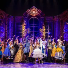 Upiór w operze: barwna scena z chórem w maskach i balowych strojach, na tle złoto-fioletowej, teatralnej scenografii.