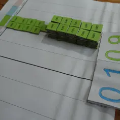 Zielone kostki z napisami "0,001" układają się w stosy, obok nich karty z liczbami 0,1 i 0,09. Nauka o ułamkach dziesiętnych.