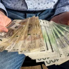 Ręce trzymające plik banknotów 200 zł i 100 zł. To darowizna od rodziców 50 tys. na nowy samochód.