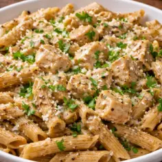Pyszne danie z makaronem pełnoziarnistym penne, kawałkami kurczaka i parmezanem, posypane świeżą natką pietruszki.