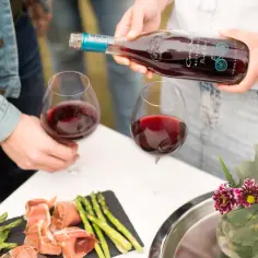 Wino Pinot Noir ma głębszy, rubinowy kolor, co pomaga odróżnić je od jaśniejszego Gamay. Na stole szparagi i prosciutto.