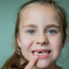 Uśmiechnięta dziewczynka z niebieskimi oczami pokazuje lukę po wypadnięciu zęba mlecznego.