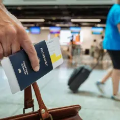Dłoń trzyma paszport USA i kartę pokładową, gotowa do podróży. Zastanawiasz się, ile za bagaż rejestrowany?