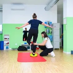 Fizjoterapeutka pomaga pacjentce ćwiczyć równowagę na poduszce balansującej, doskonaląc czucie głębokie.