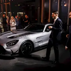 Srebrny Mercedes-AMG GT Black Series prezentowany na evencie. Ludzie w garniturach i strojach wieczorowych oglądają auto.
