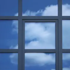 Szkło odbija błękitne niebo z chmurami. Geometryczny podział tafli tworzą ciemne szprosy, nadając budynkowi nowoczesny wygląd.