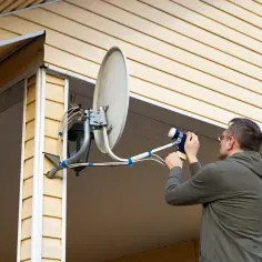 Mężczyzna reguluje antenę satelitarną. Czy antena satelitarna działa bez dekodera? To pytanie, na które odpowiedź zależy od typu sygnału.