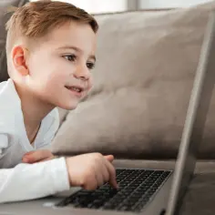 Chłopiec uczy się jak przejść na nauczanie domowe, korzystając z laptopa na kanapie.