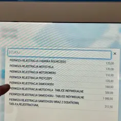 Palec wskazuje na ekranie cennik usług, gdzie widać ile kosztuje przerejestrowanie samochodu, motocykla i innych pojazdów.