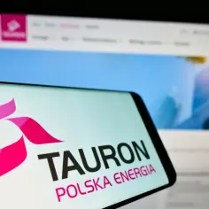 Logo Tauron Polska Energia na ekranie telefonu. W tle widać stronę internetową firmy, gdzie można sprawdzić tauron taryfy.