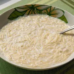 Zupa mleczna z makaronem, podana w misce z motywem kwiatowym, na zielonej podkładce.