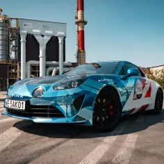 Błękitno-białe Alpine A110S z numerem 290 na tle przemysłowej zabudowy.