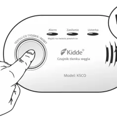Dłoń naciska przycisk "TEST/RESET" czujnika czadu Kidde K5CO, który trzeszczy, sygnalizując alarm.