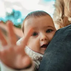 Pięciomiesięczne dziecko, wtulone w ramię, wyciąga rączkę. To pokazuje, co potrafi 5 miesięczne dziecko – ciekawość świata!