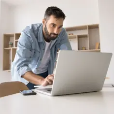 Mężczyzna w dżinsowej koszuli pracuje na laptopie, szukając nowych możliwości zatrudnienia.