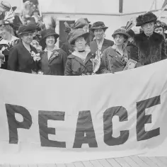 Kobiety z transparentem "PEACE" symbolizują emancypację kobiet i pozytywizm, dążąc do pokoju i równości.