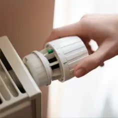 Dłoń reguluje termostat grzejnika. Co zrobić jak grzejnik grzeje do połowy? Sprawdź ustawienia pokrętła.