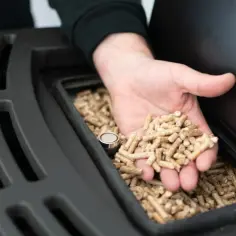 Dłoń wsypuje pellet do zasobnika pieca na pellet.