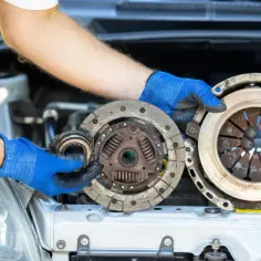 Mechanik w niebieskich rękawiczkach pokazuje zużyte części sprzęgła. Zastanawiasz się, ile kosztuje naprawa sprzęgła?