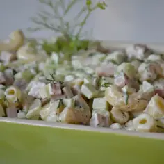 Pyszna sałatka z makaronem, szynką, ogórkiem i serem, udekorowana świeżym koperkiem.