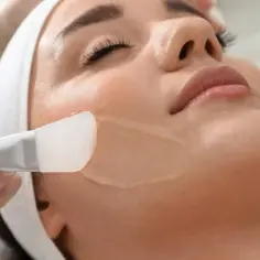 Kosmetyczka aplikuje delikatny peeling chemiczny na twarz klientki.