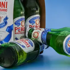 Butelki Peroni Nastro Azzurro leżą obok kartonu. Widać osad białkowy, efekt trzymania piwa w zamrażarce zbyt długo.