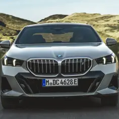 Nowe BMW 5 na krętej drodze wśród wzgórz. Elegancka sylwetka i charakterystyczny grill.
