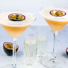 Dwa drinki z marakują, ozdobione połówkami owocu, stoją obok kieliszków z wodą.