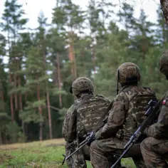 Żołnierze w kamuflażu siedzą w lesie, gotowi do służby. Czy po służbie przygotowawczej można zostać żołnierzem zawodowym? To pytanie zadaje sobie wielu.