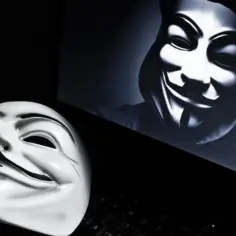 Maska Guy Fawkes leży na klawiaturze obok ekranu z podobną maską. Symbolizuje anonimowego hakera.