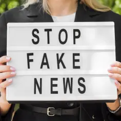 Kobieta trzyma tablicę z napisem "STOP FAKE NEWS", walcząc z dezinformacją.