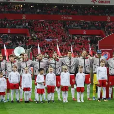 Piłkarze reprezentacji Polski i dzieci stoją na murawie stadionu, w tle trybuny z kibicami.
